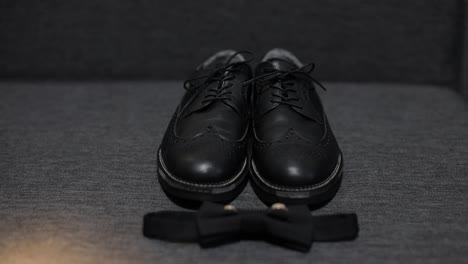 Wedding-details-of-groom.-Bridegrooms-black-bow-tie,-shoes-and-wedding-rings-lie-on-sofa