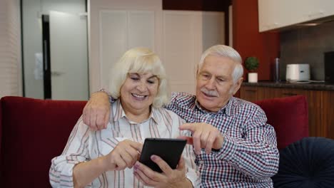 Senior-old-couple-grandparents-talking-and-using-digital-tablet-computer-at-home.-Internet-shopping