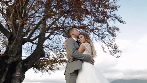 Lovely-young-newlyweds-bride-groom-embracing-on-cloudy-sky-background,-wedding-couple-family-in-love