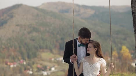 Newlyweds.-Caucasian-groom-with-bride-ride-a-rope-swing-on-a-mountain-slope