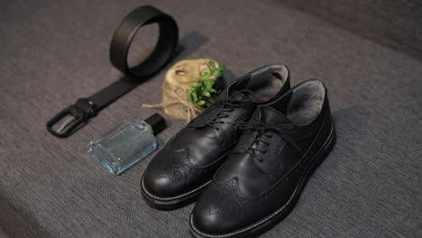 Detalles-De-La-Boda-Del-Novio.-El-Perfume,-El-Cinturón,-Los-Zapatos-Y-Los-Anillos-De-Boda-Del-Novio-Yacen-En-El-Sofá.