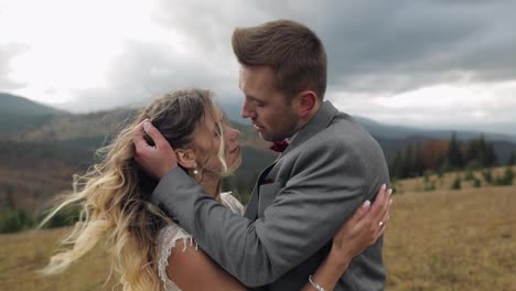 Lovely-young-newlyweds-bride-and-groom-embracing,-making-a-kiss-on-mountain-slope,-wedding-couple