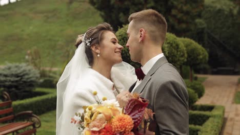 Lovely-newlyweds-caucasian-bride-embracing-groom-in-park-making-kiss,-wedding-couple-family-hugging