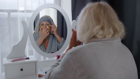 Old-senior-woman-grandmother-taking-care-of-skin-near-eyes-and-wrinkles,-putting-makeup-on-at-home