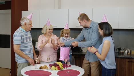 Mother,-father-and-grandparents-giving-gift-bag-for-child-girl.-Celebrating-birthday-anniversary