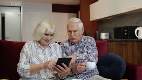 Pareja-De-Jubilados-Mayores-Con-Tableta-Digital-En-Casa.-Descansando-En-El-Sofá-En-La-Acogedora-Sala-De-Estar