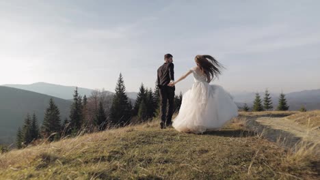 Newlyweds.-Caucasian-groom-with-bride-running-on-mountain-slope.-Wedding-couple