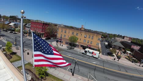 Luftaufnahme-Der-Amerikanischen-Flagge-In-Einer-Kleinstadt-Mit-Einem-Fahrenden-FedEx-LKW-Auf-Der-Hauptstraße