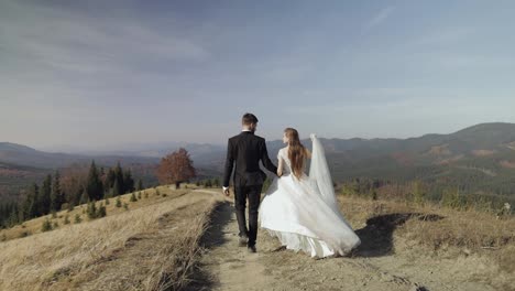 Newlyweds.-Caucasian-groom-with-bride-walking-on-mountain-slope.-Wedding-couple