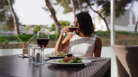 Köstliches-Abendessen-Am-Tisch-Im-Freien-Und-Frau-Trinkt-Wein-Im-Hintergrund,-Mallorca