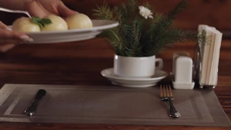 Hands-of-waiter-puts-plate-with-traditional-dish-Gombovtsi-Cheese-Dumplings-on-table-in-cafe