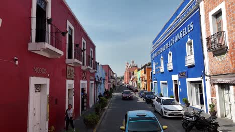 Backwards-low-altitude-flight-overlooking-colorful-houses,-people-and-cars-in-Atlixco,-Puebla