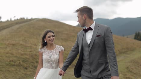 Lovely-young-newlyweds-bride-groom-walking-on-mountain-slope,-holding-hands,-wedding-couple-family