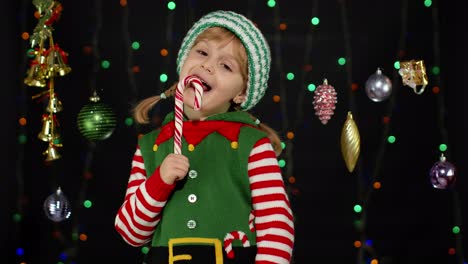 Kid-girl-in-Christmas-elf-Santa-Claus-helper-costume-licking-candy-cane-lollipop-caramel-sweets