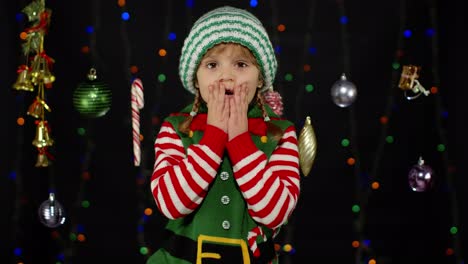 Kid-girl-in-Christmas-elf-Santa-Claus-helper-costume.-Child-doing-winner-gesture,-wawing-hands