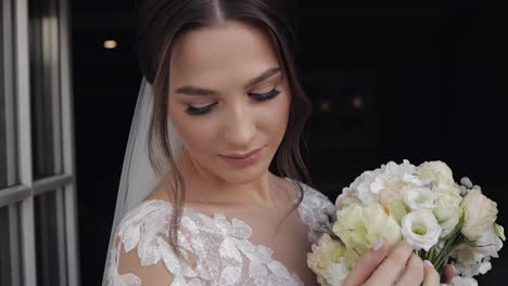 Bride-in-wedding-dress-and-veil-with-bouquet-of-flower-from-groom-stay-near-balcony-doors-at-home