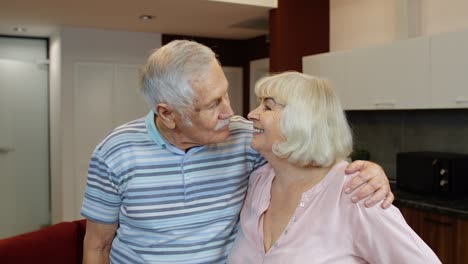 Senior-couple-retired-grandparents-husband-and-wife-happy-faces-embracing-at-home,-hugging,-laughing