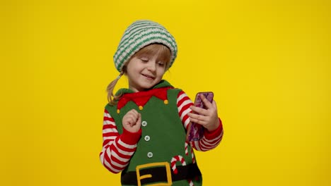 Kid-child-girl-in-Christmas-elf-Santa-Claus-helper-costume-making-a-video-call-on-mobile-phone