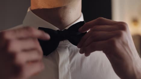 Groom-adjusts-bow-tie,-preparing-to-go-to-the-bride,-businessman-in-white-shirt,-wedding-day