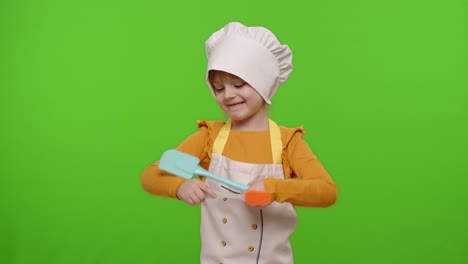 Child-girl-dressed-in-apron-like-chef-cook-dancing-spatula-on-chroma-key-background,-slow-motion