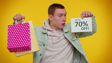 Cheerful-teen-man-showing-shopping-bags-and-Up-To-70-Percent-Off-inscriptions-banner,-Black-Friday