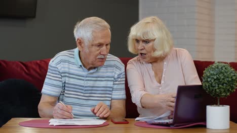 Stressed-senior-couple-discuss-unpaid-bank-debt-holding-bills,-doing-paperwork,-planning-budget