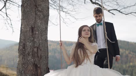 Newlyweds.-Caucasian-groom-with-bride-ride-a-rope-swing-on-a-mountain-slope