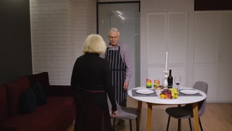 Senior-retired-couple-having-fun-during-romantic-supper-in-the-kitchen-celebrating-their-anniversary