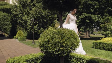 Hermosa-Y-Encantadora-Novia-Elegante-Con-Vestido-De-Novia-Blanco-Y-Velo-Caminando-En-El-Parque-Y-Esperando-Al-Novio