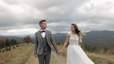 Lovely-caucasian-wedding-newlyweds-family-bride-groom-holding-hands,-making-a-kiss-on-mountain-slope