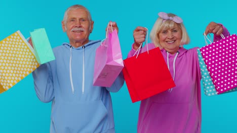 Senior-grandmother-grandfather-showing-shopping-bags,-advertising-price-discounts,-Black-Friday-sale