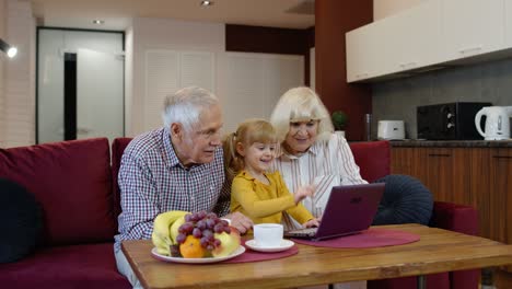 Senior-Caucasian-couple-with-child-girl-granddaughter-using-a-laptop-computer,-watching-funny-videos