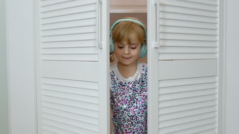 Little-child-girl-wearing-headphones-listening-to-music-and-funnily-dancing-near-wardrobe-at-home