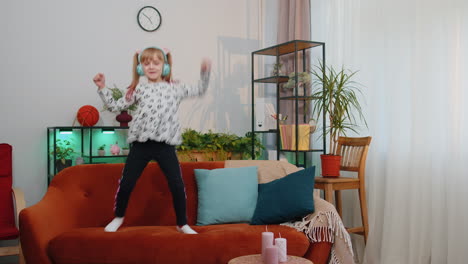 Happy-child-girl-kid-in-headphones-dancing-and-jumping-while-listening-to-the-music-at-home-alone