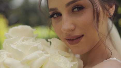 Beautiful-stylish-bride-in-white-wedding-dress-and-veil-holding-wedding-bouquet-in-hands-in-park