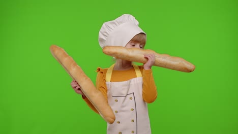 Child-girl-cook-chef-baker-in-apron-and-hat-sniffing-two-baguettes,-fooling-around,-making-faces