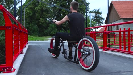 Footage-of-a-man-riding-his-chopper-styled-black-bike-or-bicycle-on-a-bridge-in-slow-motion-with-whitewall-wheels-and-stopping