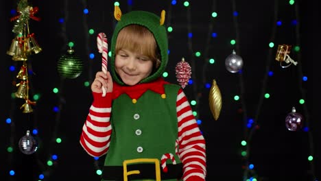 Kid-girl-in-Christmas-elf-Santa-Claus-helper-costume-with-candy-cane-lollipop-joyful-smiling