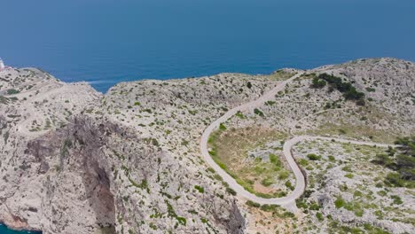 Picturesque-aerial-view-of-serpentine-road-leading-to-lighthouse,-Mallorca