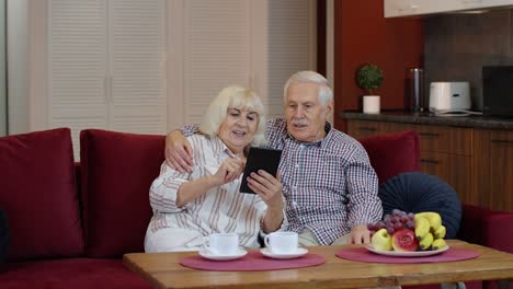 Pareja-De-Jubilados-Mayores-Con-Tableta-Digital-En-Casa.-Descansando-En-El-Sofá-En-La-Acogedora-Sala-De-Estar