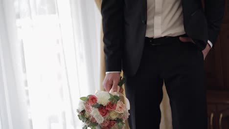 Groom-with-wedding-bouquet-in-his-hands-at-home.-White-shirt,-jacket