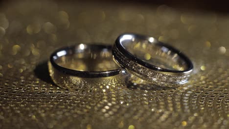 Wedding-rings-lying,-rotate,-spinning-on-shiny-golden-shining-surface-with-light,-close-up-macro