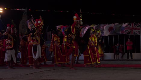 Cultural-dancing-of-a-group-in-unique-costumes-at-the-Nias-Pro-Surf-Competition,-windy-flags-in-the-background