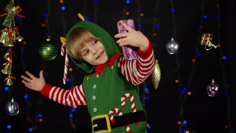 Kid-girl-in-Christmas-elf-Santa-helper-costume-making-selfie-on-mobile-phone.-New-Year-holidays