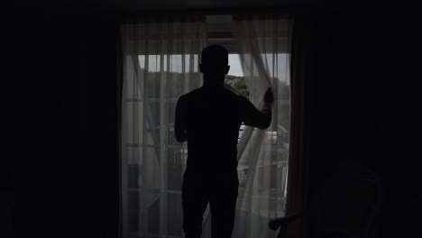 Handsome-groom-in-gray-jacket-goes-to-balcony-and-opens-curtains-in-hotel-room-or-home-apartment