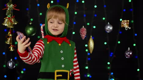 Kid-child-girl-in-Christmas-elf-Santa-Claus-helper-costume-making-a-video-call-on-mobile-phone