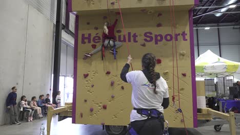 Slow-motion-shot-of-a-girl-climbing-on-a-wall-guided-by-a-worker