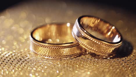 Wedding-rings-lying,-rotate,-spinning-on-shiny-golden-shining-surface-with-light,-close-up-macro