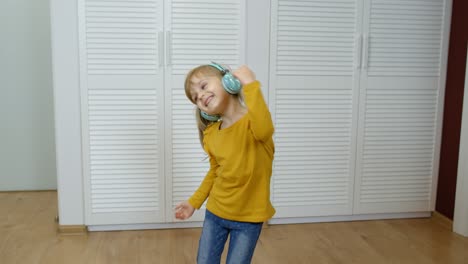 Little-child-girl-wearing-headphones-listening-to-music-and-funnily-dancing-near-wardrobe-at-home