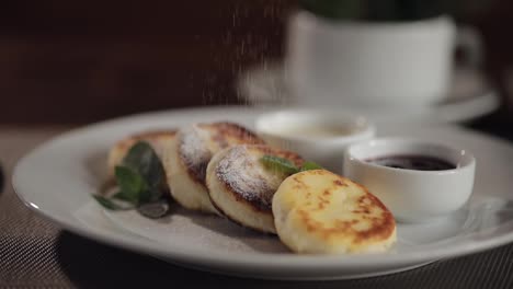 Chef-sprinkling-sugar-powder-on-tasty-delicious-cottage-cheese-peach-pancakes-on-plate-on-table